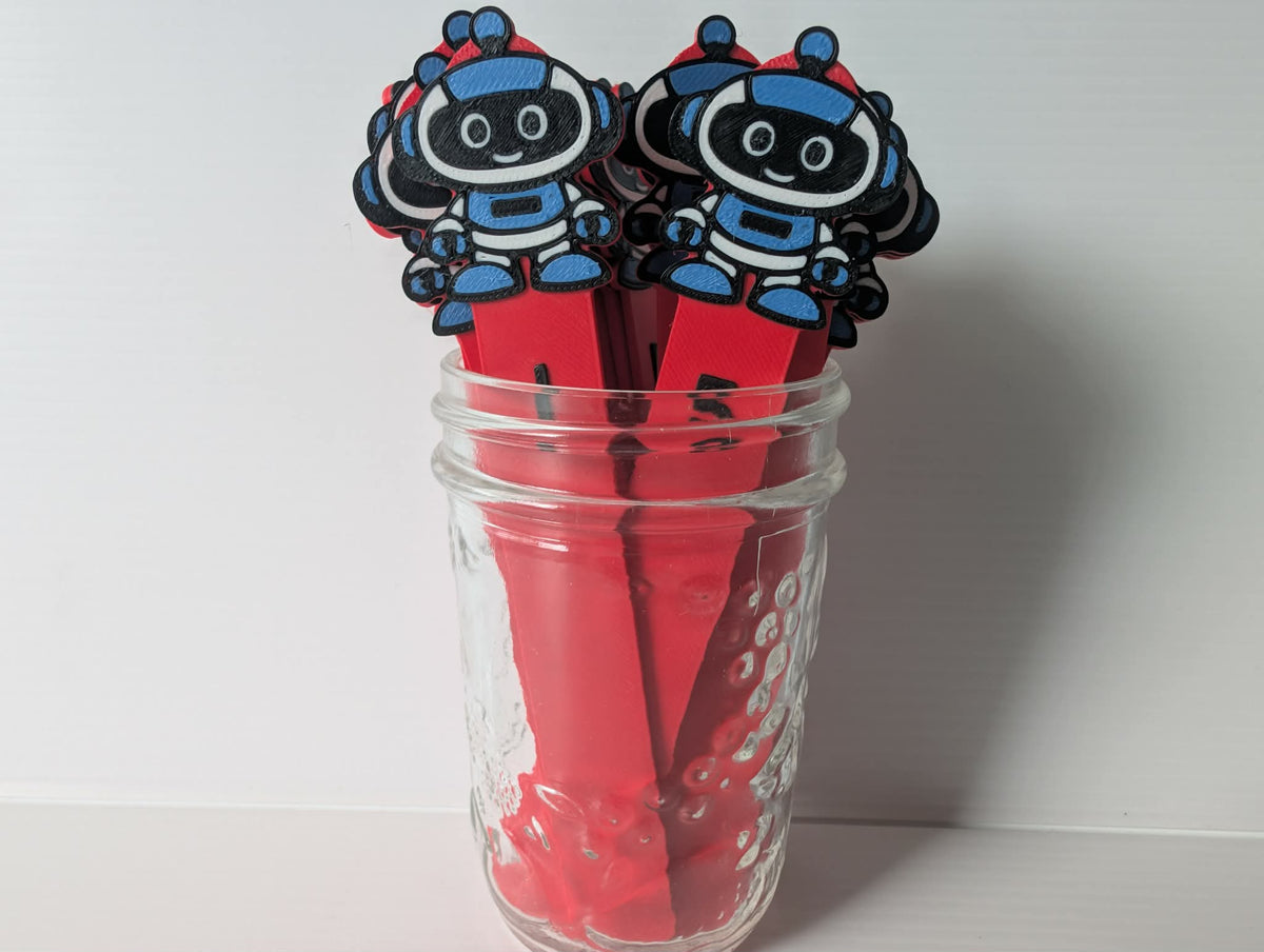 Bâtons de pige modèle robot : bâtons rouges surmontés d'un petit robot bleu, noir et blanc, dans un pot de verre