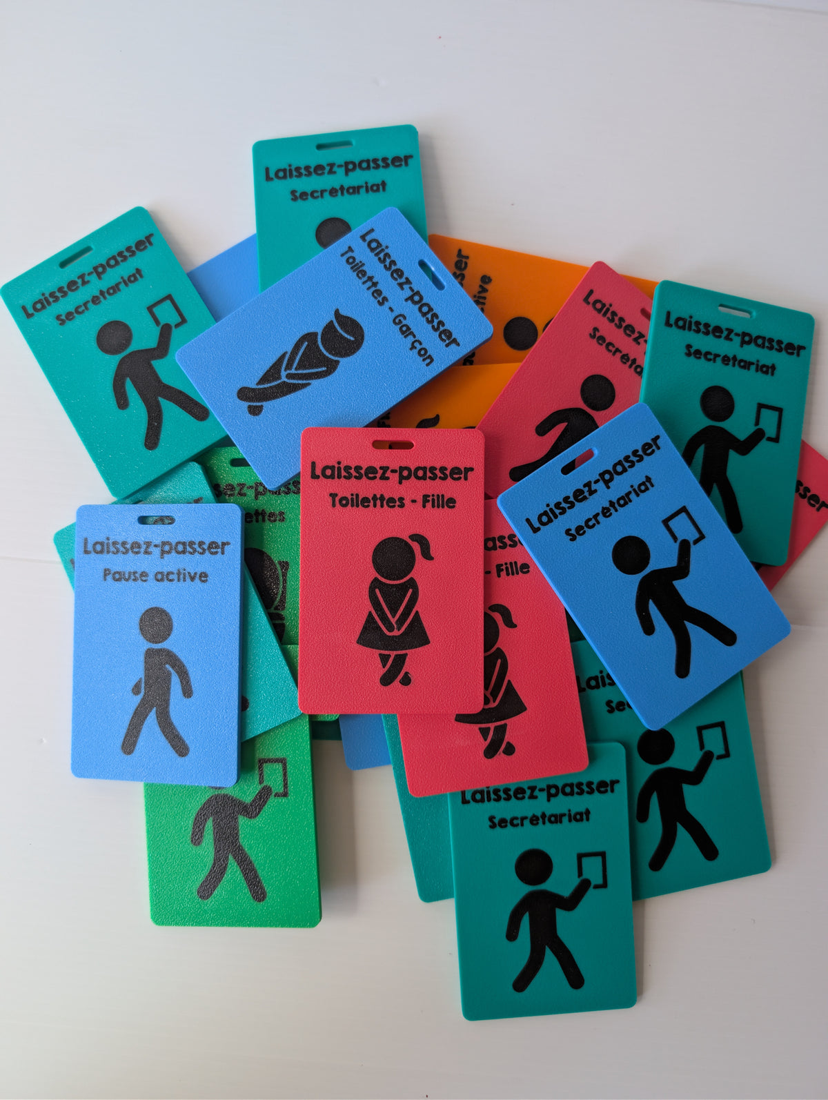Pile de laissez-passer colorés à pictogrammes noirs, dont les modèles secrétariat, toilettes garçon, toilettes fille et pause active